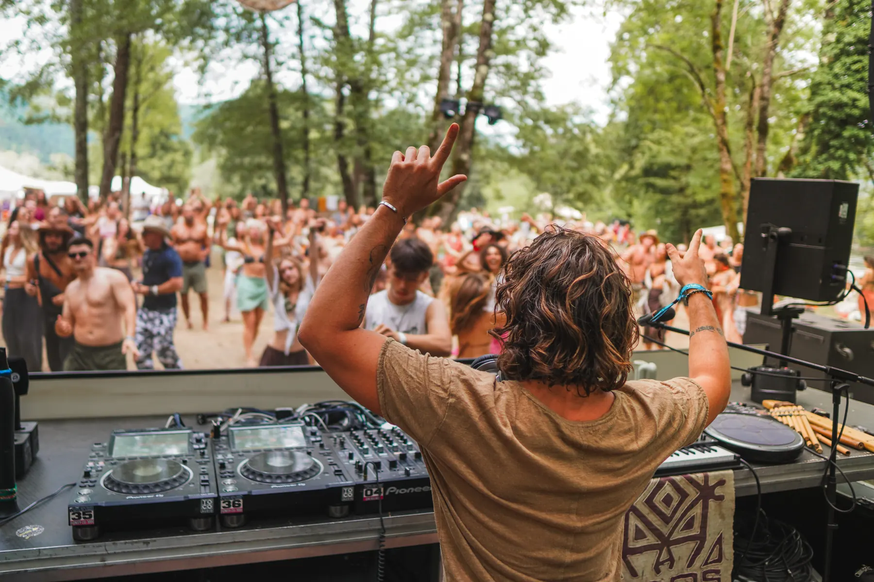 Jasileo with arms raised behind the decks, facing a dancing crowd at Guardians Festival, Slovenia